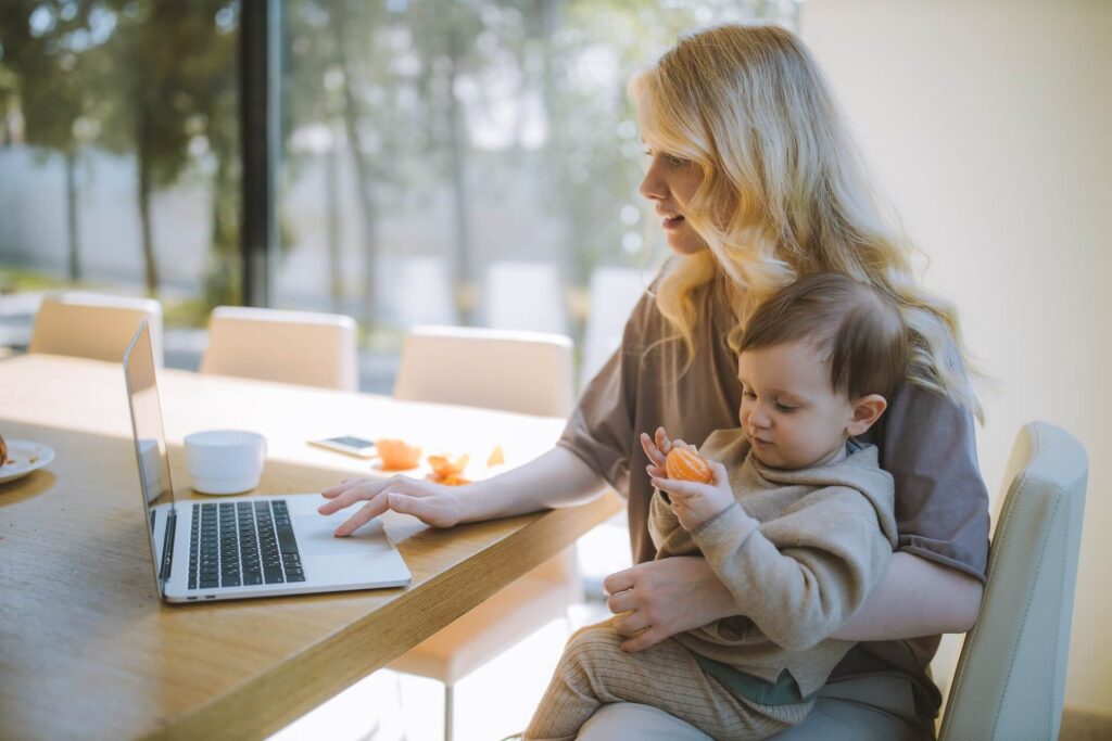 Mother working on laptop while holding a toddler sitting on her lap